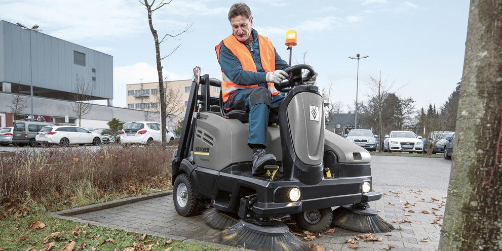 Eine Person sitzt auf einer Aufsitz-Kehrsaugmaschine von Kärcher und reinigt einen Parkplatz