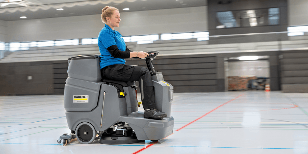 Mann sitzt auf Kehrmaschine und kehrt Boden.