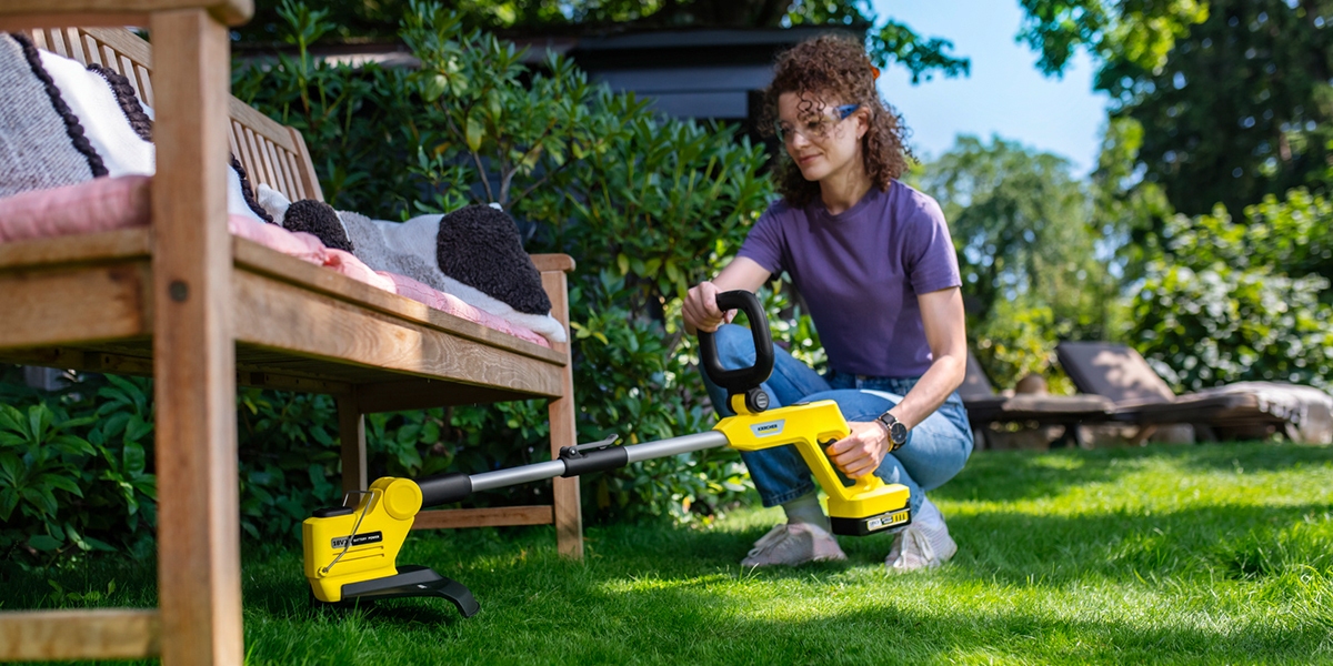 Person trimming underneath a bench with the Kärcher battery lawn trimmer