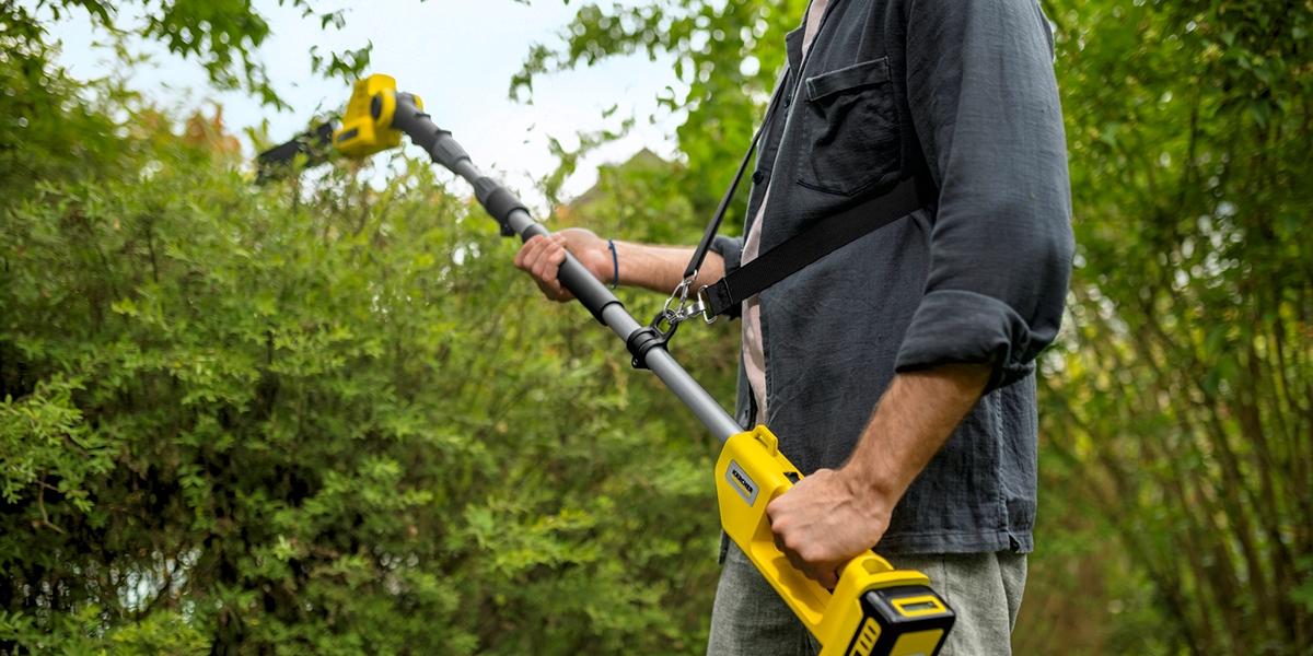 Person using the shoulder strap on the Kärcher battery pole hedge trimmer