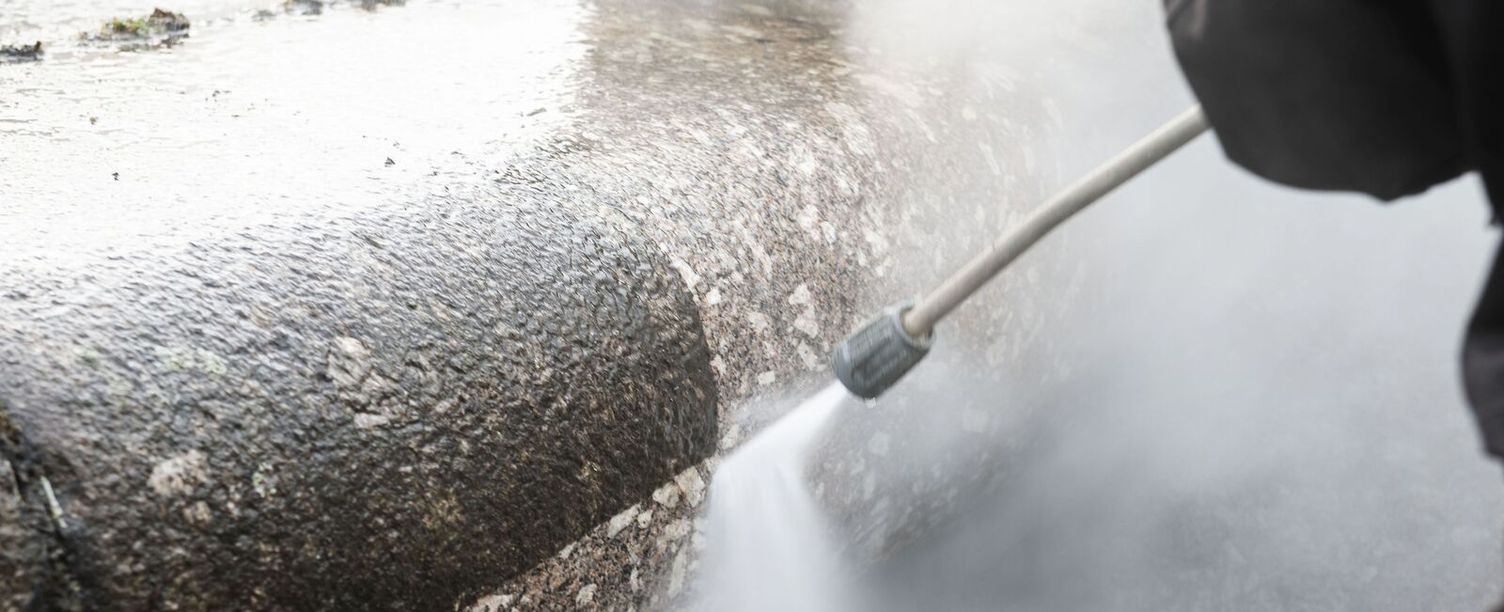 A natural stone facade is being cleaned with a pressure washer. 