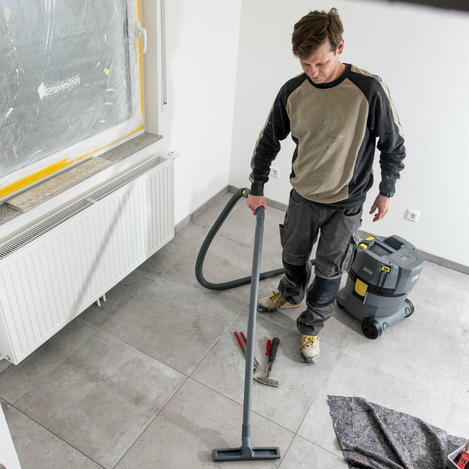 A person cleans a dirty floor in a newly renovated room with a Kärcher Battery Wet and Dry Vacuum Cleaner