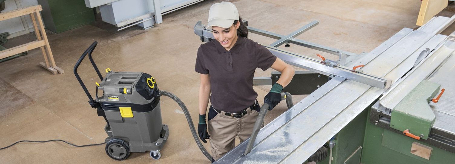 A person cleans the workbench of a machine using a Kärcher Vacuum Cleaner