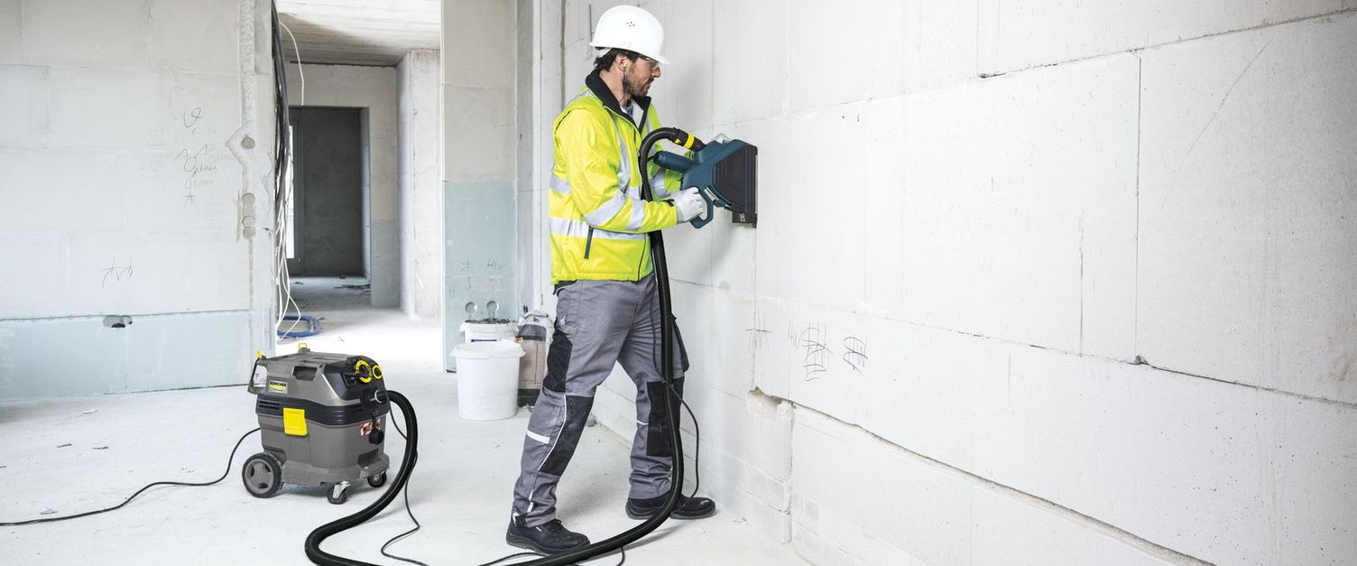 A person in protective clothing cleans a wall in the shell with a safety vacuum cleaner.