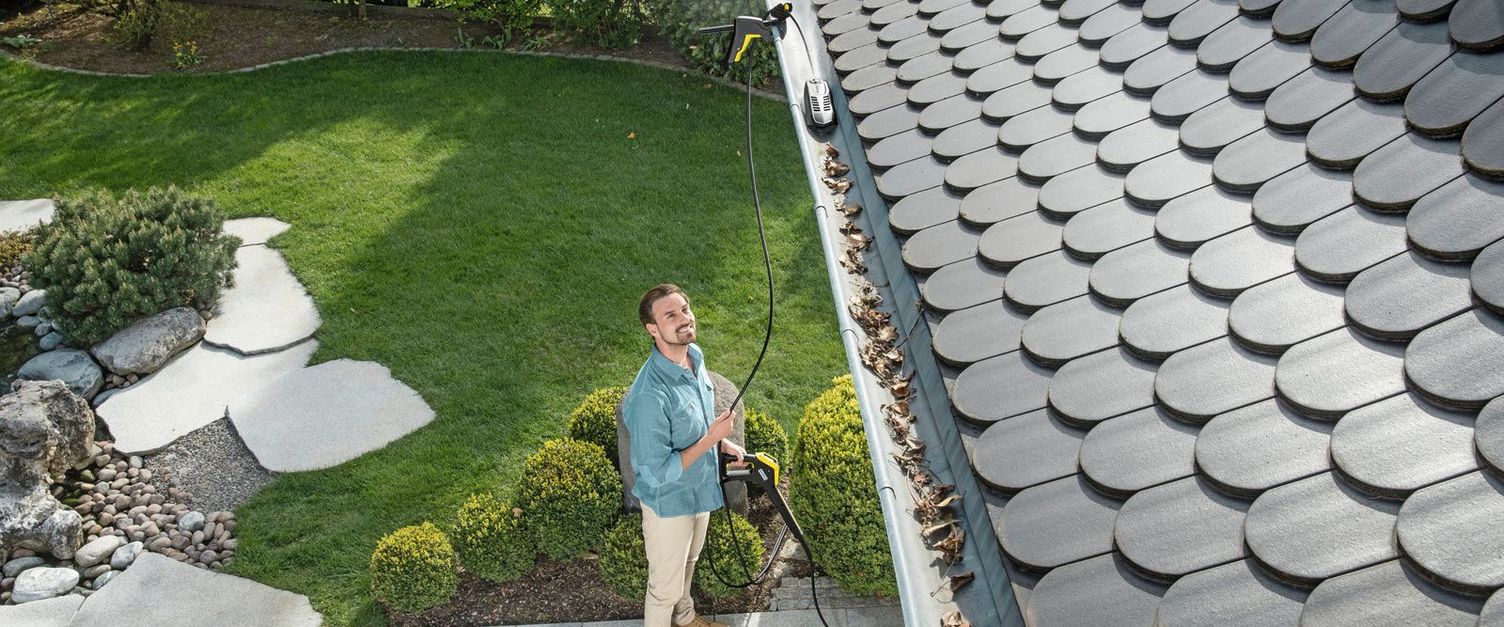 A man stands in the garden cleaning the gutter of his house with a Kärcher device