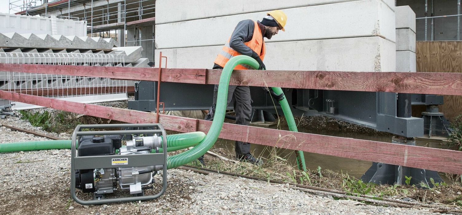 A person vacuums dirty water out of an excavation trench with a green pipe and a Kärcher Wastewater Pump