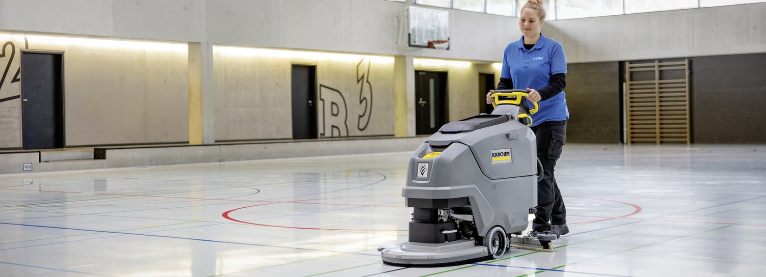 A woman cleaning the floor of a gym with a disc brush model.