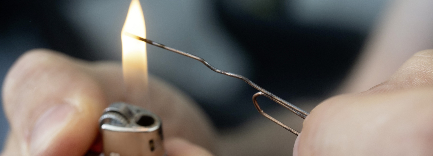 A bent paperclip is being heated with a lighter.