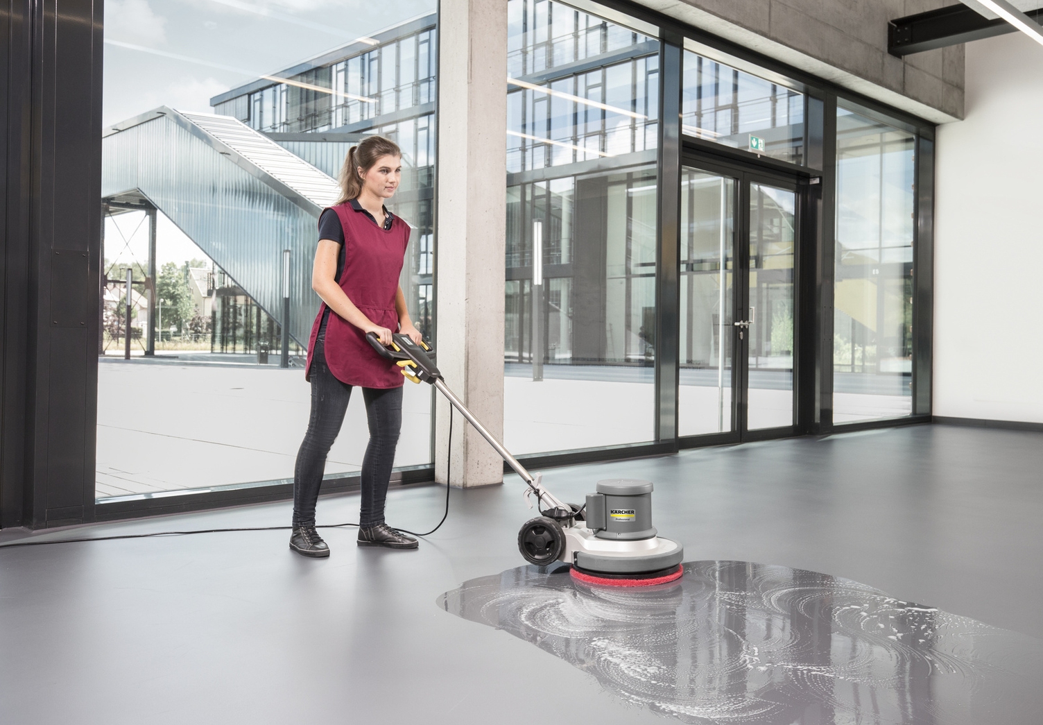 A woman cleaning the floor of an entrance area with a scrubber dryer.