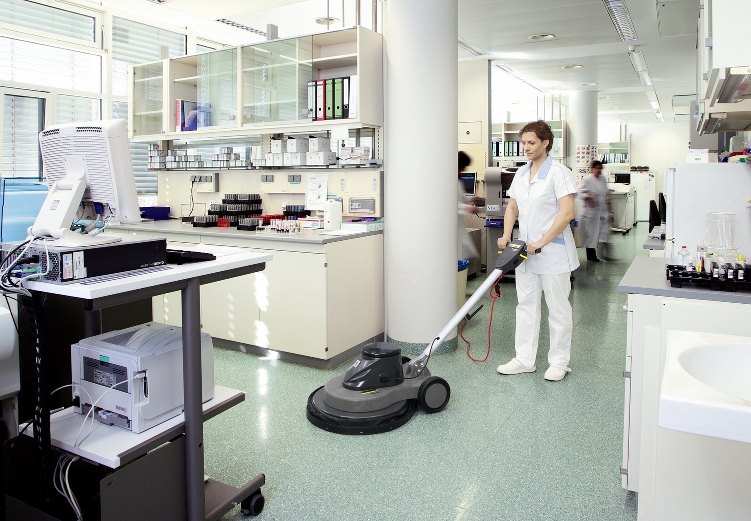 A woman operating a Kärcher scrubber dryer on resilient floor covering.