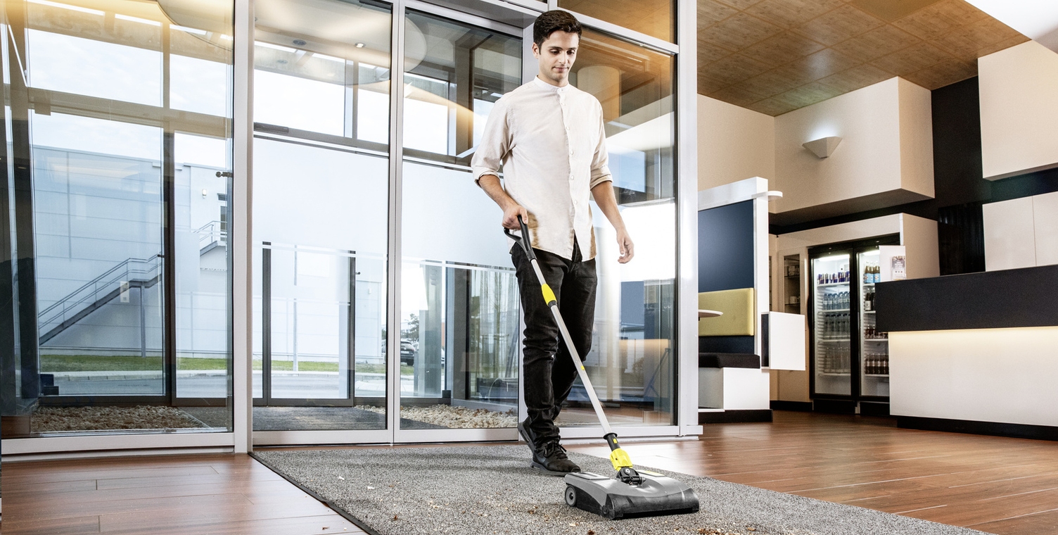 Electric broom in use A person cleaning a carpet runner in the entrance area with the electric broom
