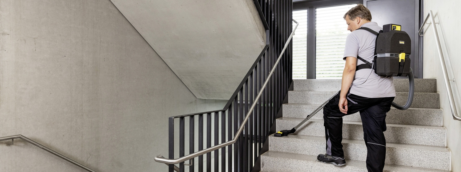 A person is vacuuming the stairs in the stairwell with a Kärcher backpack vacuum cleaner