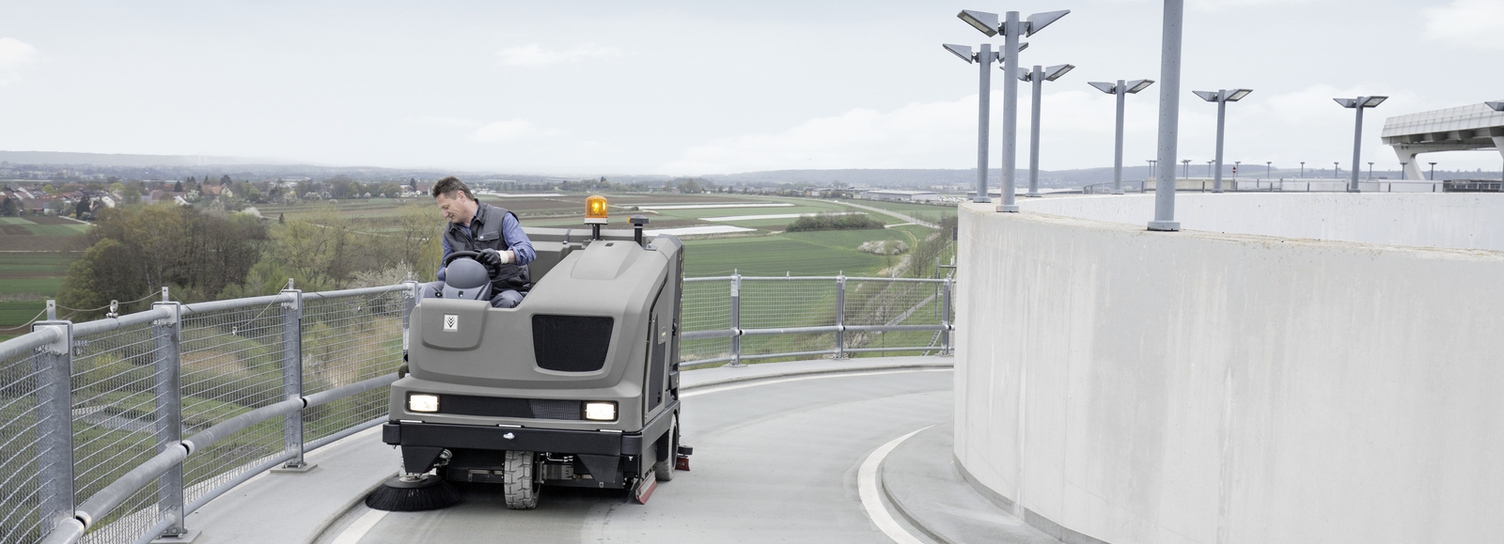 A person driving up the road of a parking deck with a Kärcher sweeper