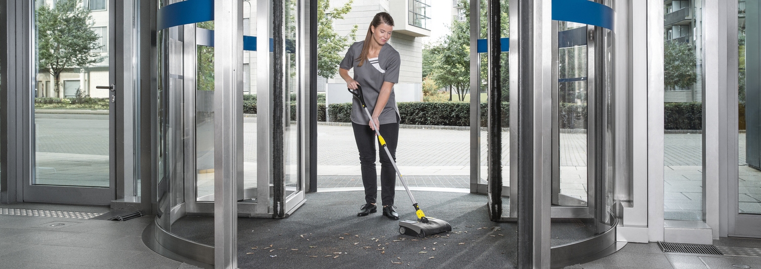 A person cleaning the floor in a revolving door with a Kärcher electric broom