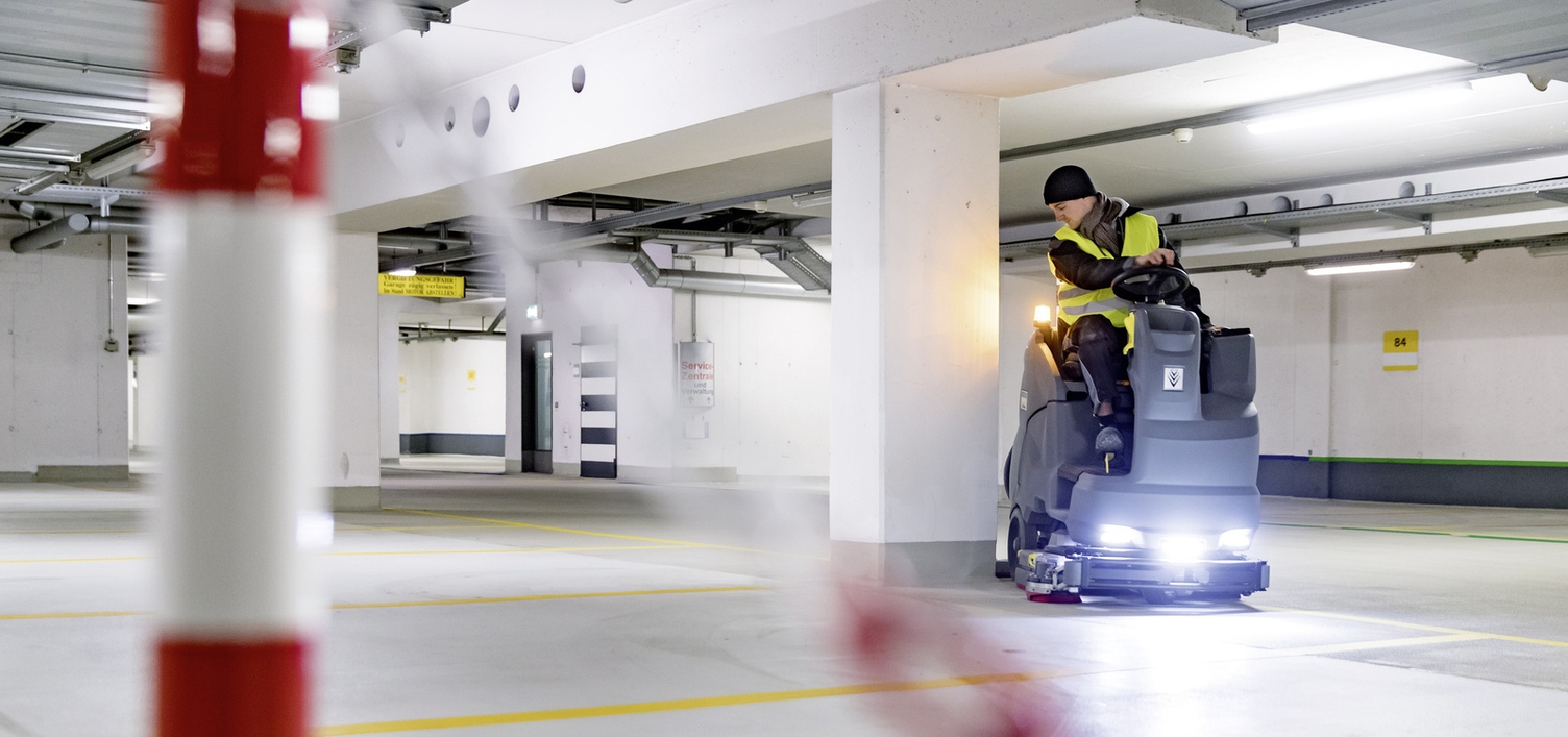 A person sits on a ride-on sweeper and cleans a parking garage