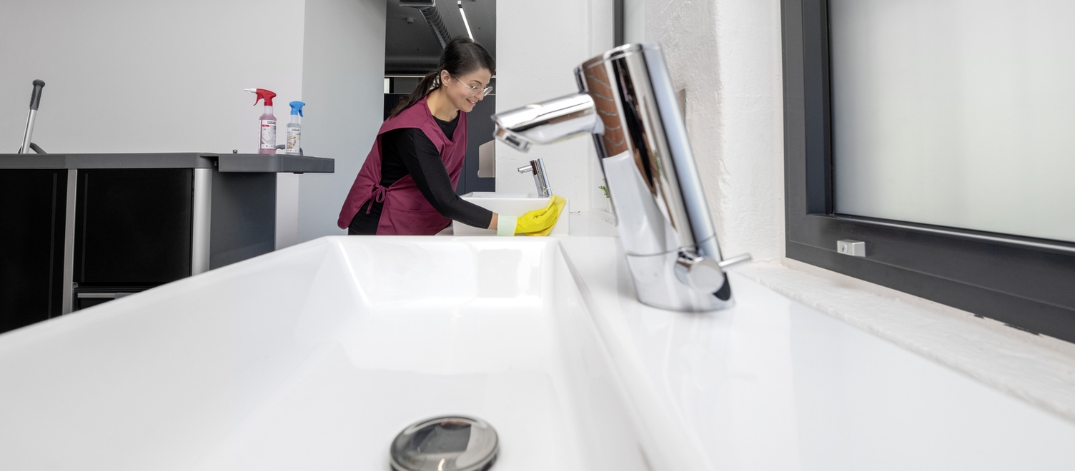 A person is cleaning the sink in a sanitary facility