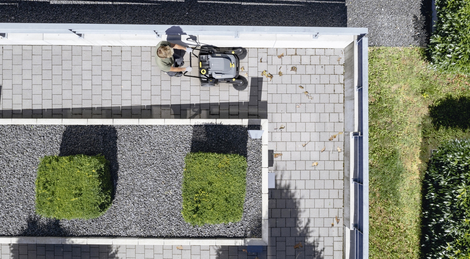 A person with a manual Kärcher sweeper cleaning a path with cobblestones