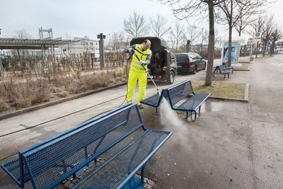 Person cleaning park bench with a high pressure cleaner Person cleaning park bench with a high pressure cleaner