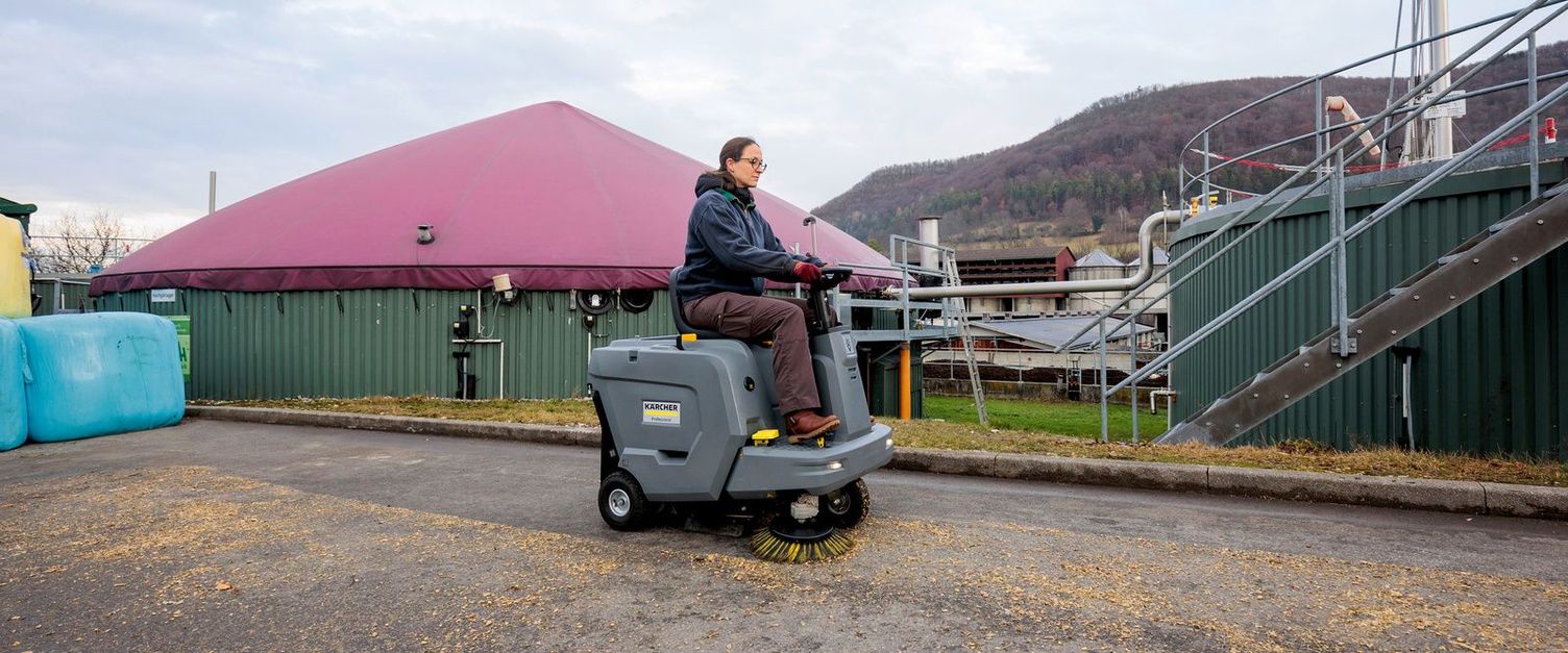 A woman driving a sweeper across a yard