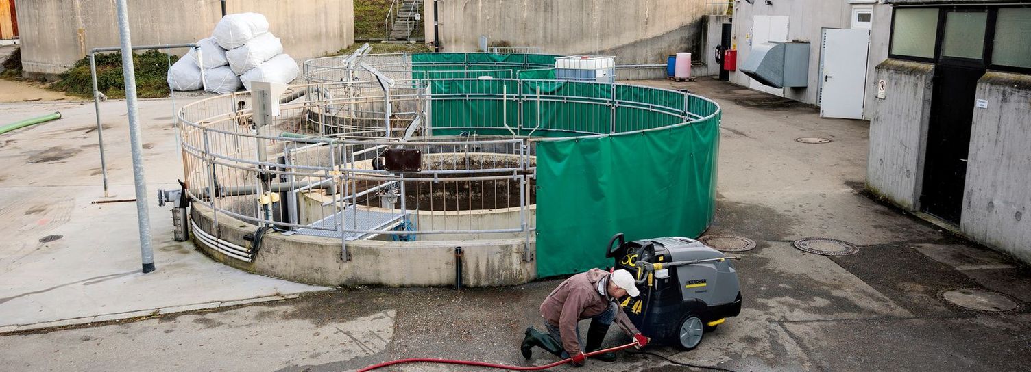 A man kneels in front of a Kärcher pressure washer by a biogas plant
