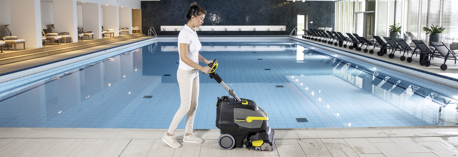A person cleans the tiles in the spa area with the help of a scrubber dryer