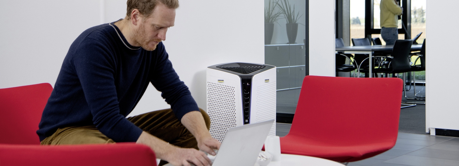 A person sits with a laptop next to an air purifier