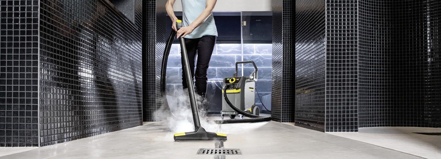 A person cleans a shower area with a steam cleaner