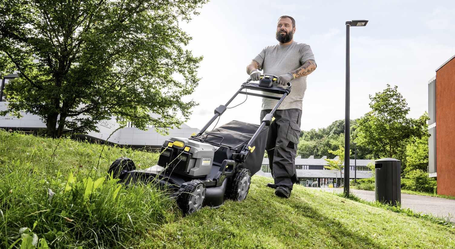 A person trimming a green area on a slope with a Kärcher lawn mower