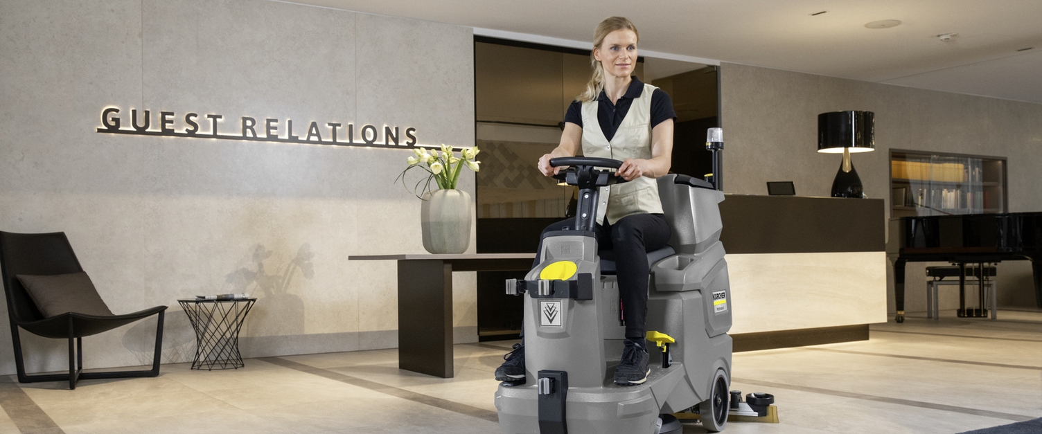A person sitting on a scrubber dryer cleaning the hotel lobby