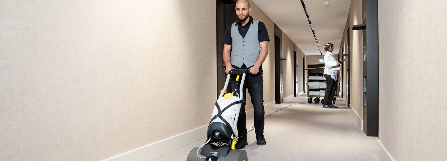 Cleaning carpets with iCapsol A man cleans a long hotel hallway carpet with a Kärcher vacuum cleaner.