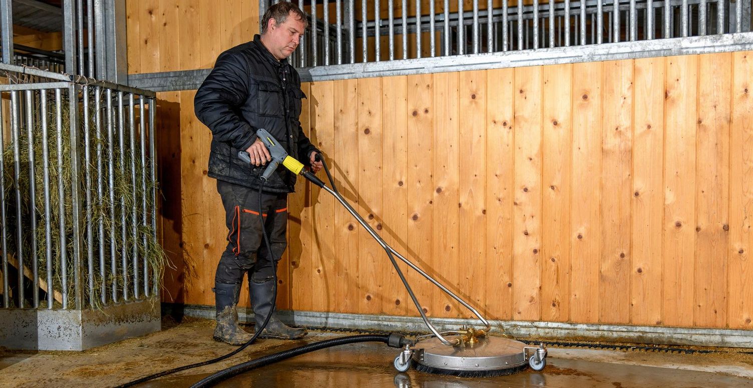 a man cleans a horse box with a Kärcher surface cleaner