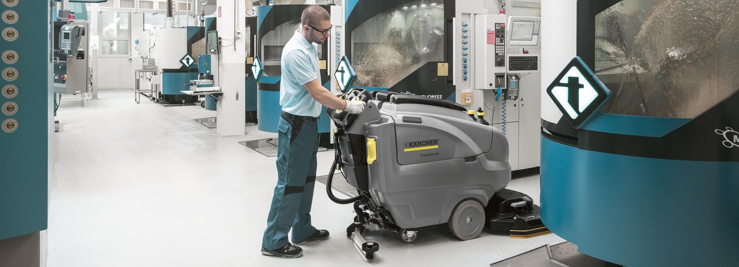 A man cleans the floor in the production hall with a scrubber-dryer