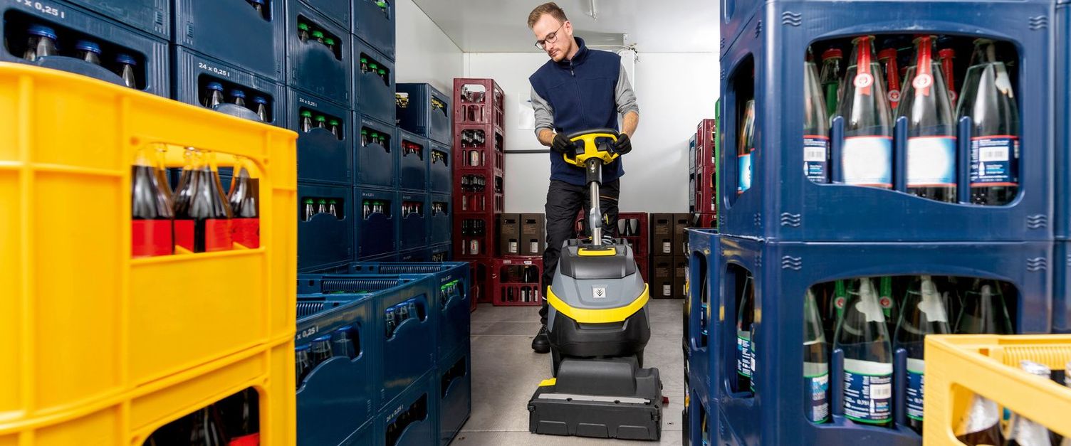 Cold room cleaning with scrubber dryer and accessories Front view of man cleaning between crates of drinks with cleaning device