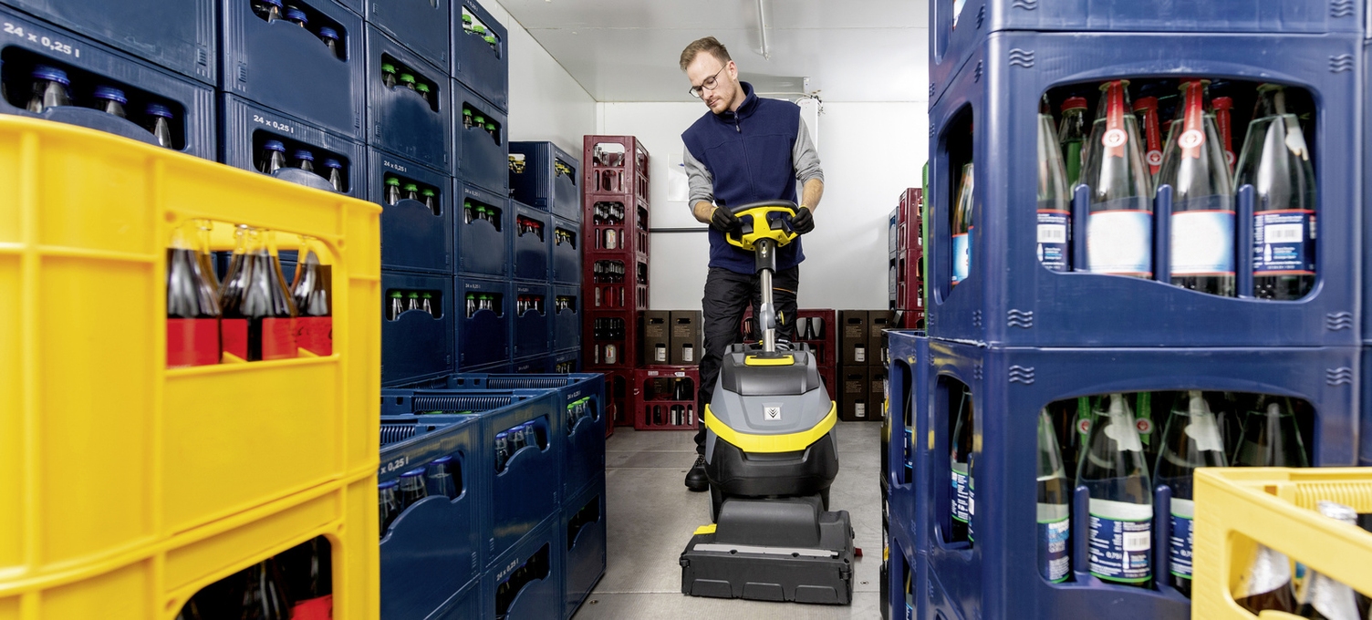 A person is cleaning a cold storage room with a scrubber dryer