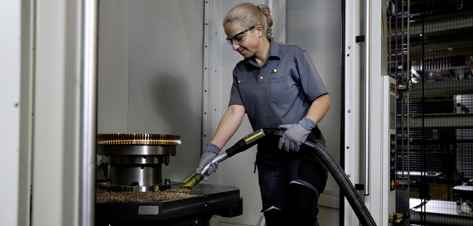 A woman vacuums metal shavings with an industrial vacuum cleaner