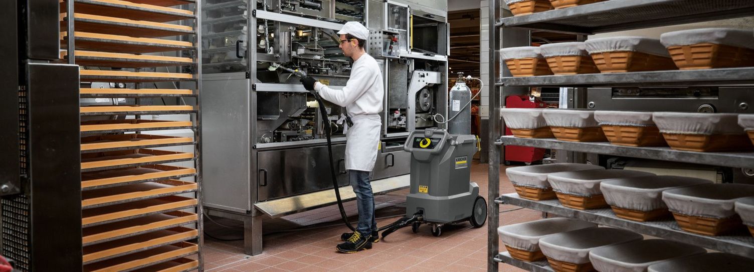 Machine cleaning in the bakery View of a baker cleaning the inside of a machine with a Kärcher dry vacuum.