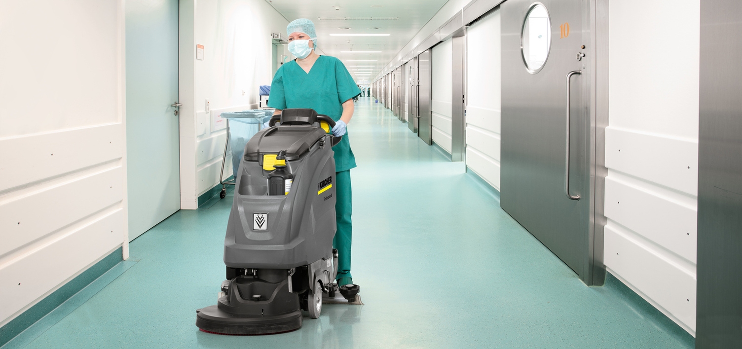 A person is cleaning the floor in the operating room area with a scrubber dryer