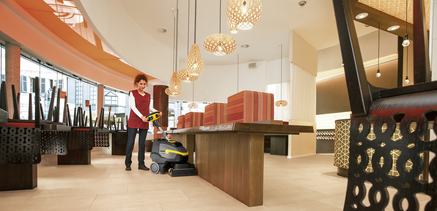 A person cleaning the floor of a restaurant with a scrubber dryer