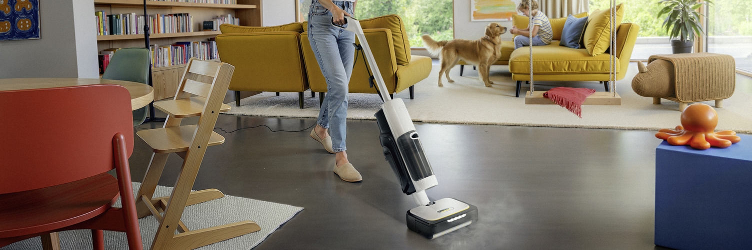 Kärcher steam vacuum cleaner cleans dark floor in living room with dog and yellow sofa.