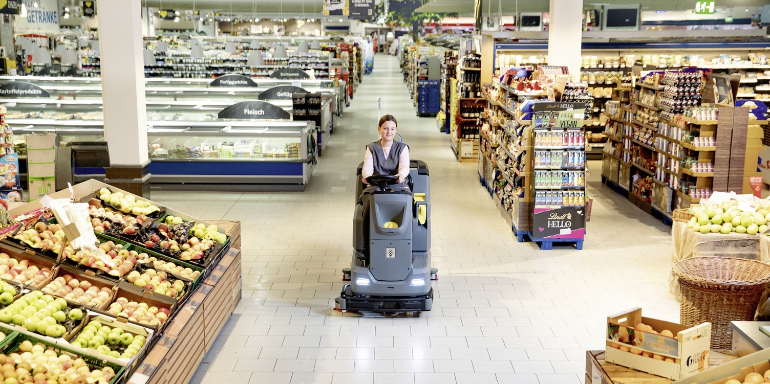 A person is cleaning the floor area of a supermarket with a scrubber dryer