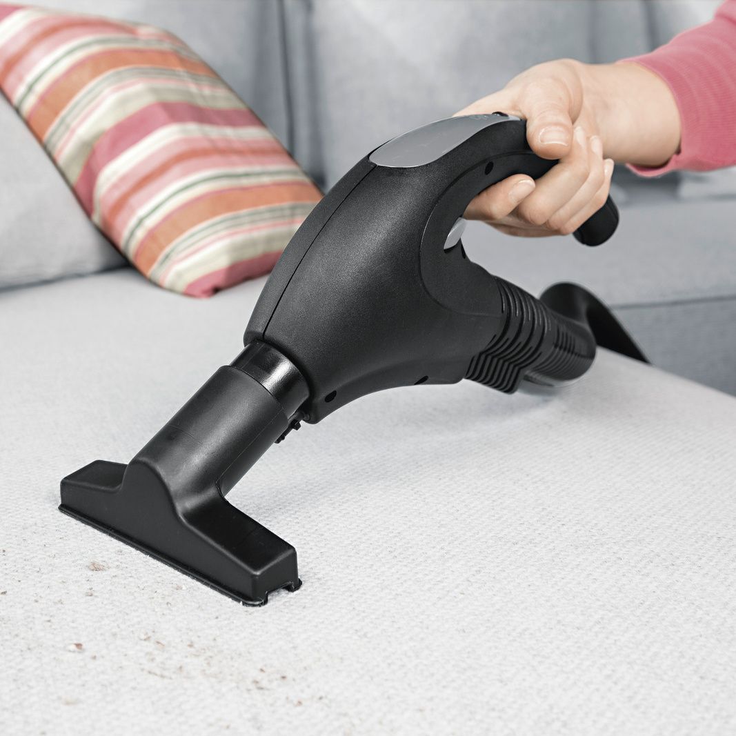 Kärcher steam vacuum cleaner upholstery nozzle thoroughly cleans dirt from a grey fabric sofa.