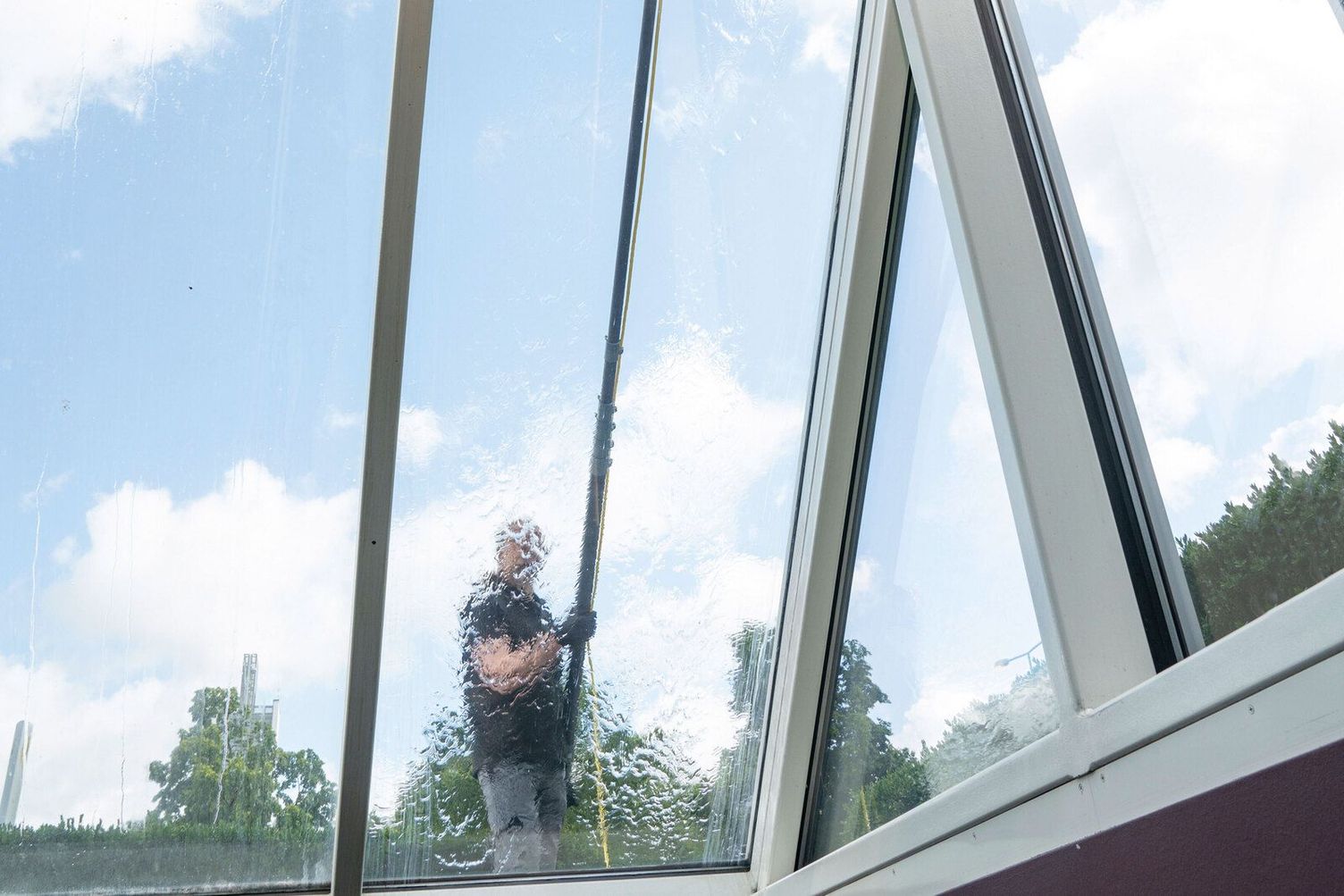 A person cleans a glass facade using a Kärcher Telescopic Spray Lance 