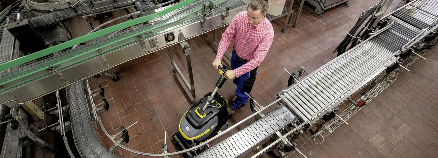 A man cleans the industrial floor where a transport belt is located