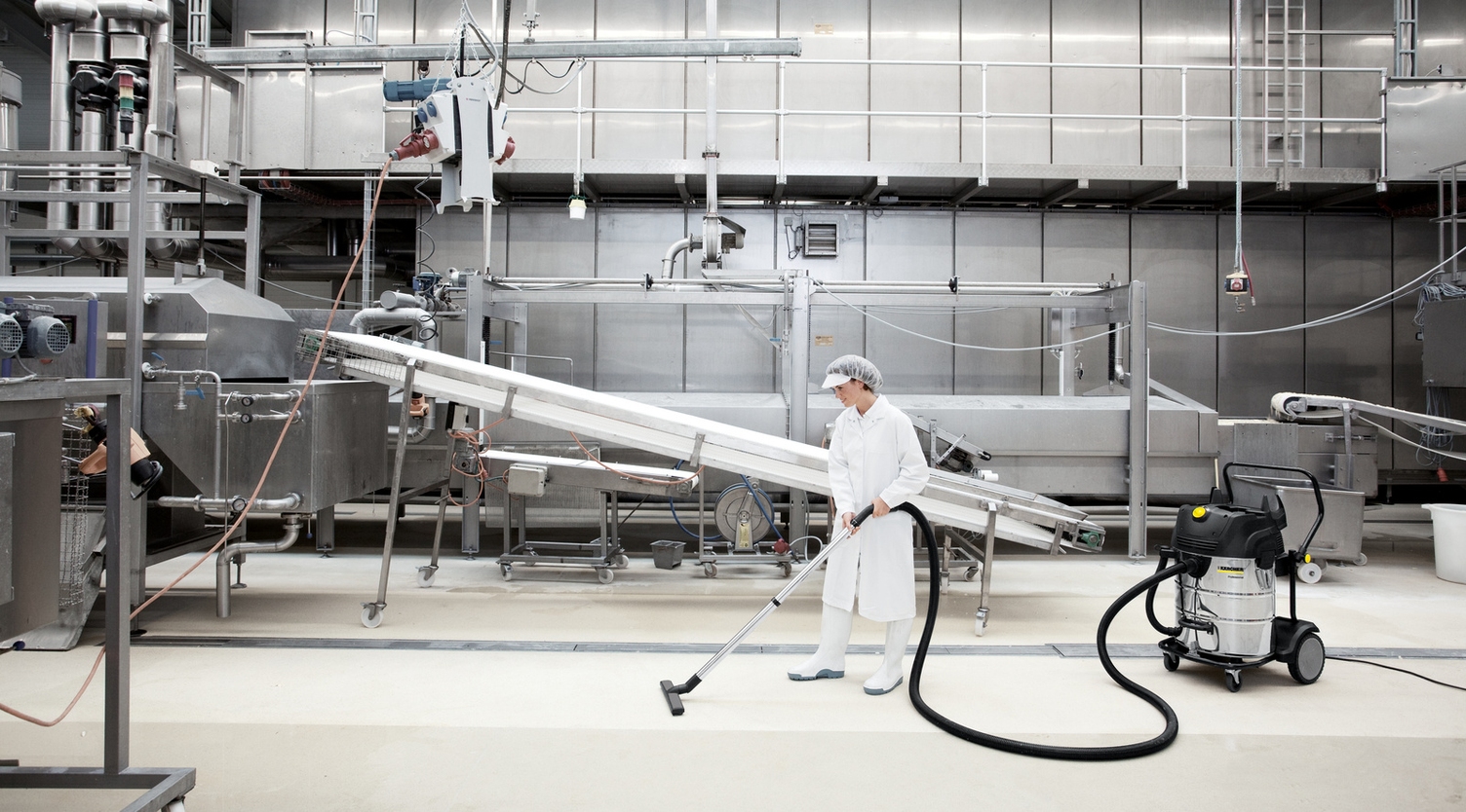  A woman cleans an industrial floor with a dry vacuum cleaner from Kärcher
