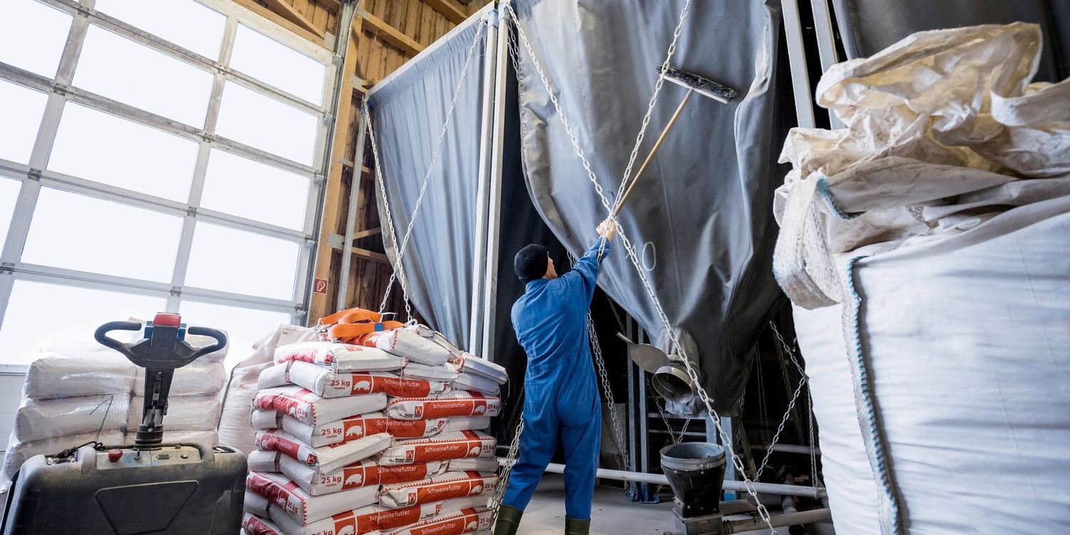 Silo cleaning A man cleaning the trevira tarpaulins in a silo with brooms. Next to him is a hand pallet truck and pallets of feed.