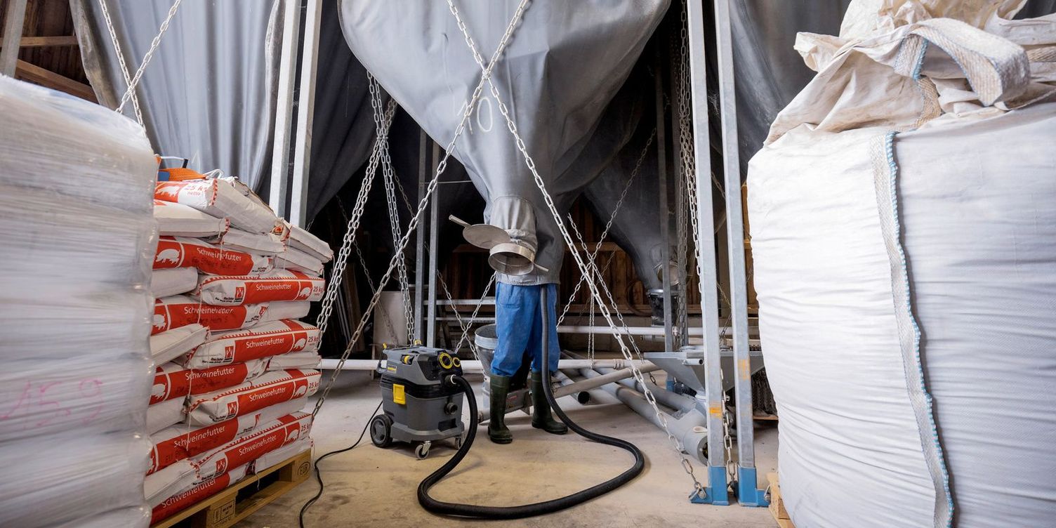 Cleaning trevira sacks Interior view of a substructure with pallets on which feed sacks are placed. In the background, a man is cleaning a trevira silo with a dry vacuum cleaner.