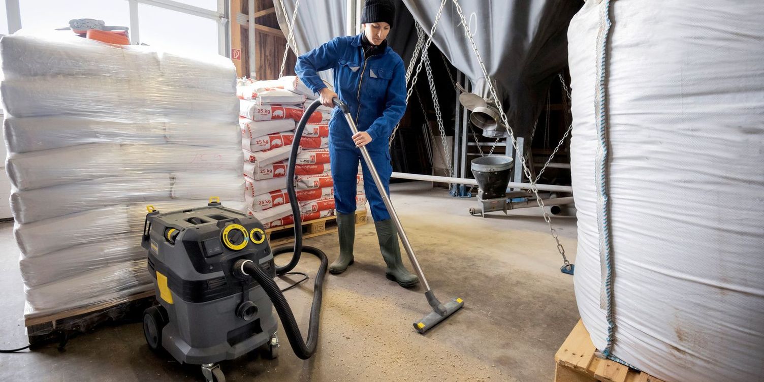 Cleaning Trevira sacks View of a man using a dry vacuum cleaner to clean the floor of an indoor space between pallets of feed bags.