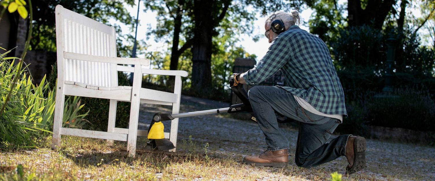 Remove weeds A man removes weeds from under a garden bench with the Kärcher weed remover