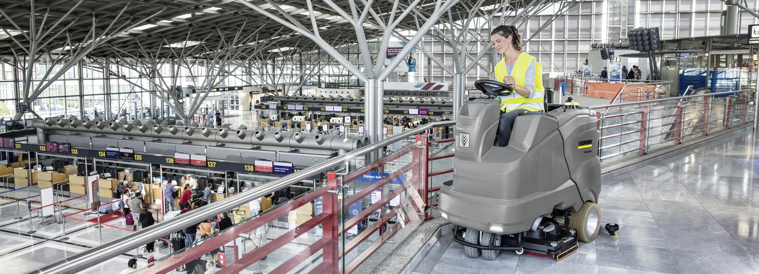 A person cleans the airport area with a ride-on scrubber-dryer from Kärcher