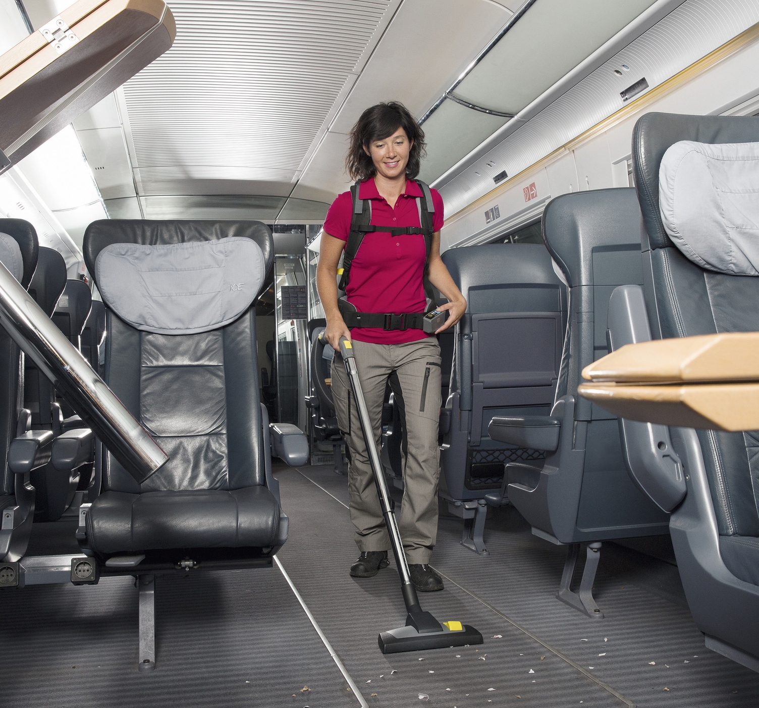 A person cleaning the interior of a train with a backpack vacuum cleaner